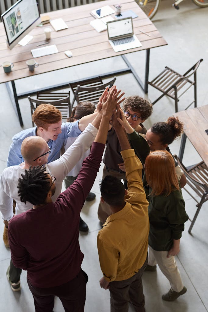 A diverse group of professionals high-fiving in a modern office, showcasing teamwork and collaboration.