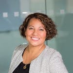 A confident woman with curly hair smiling in an office environment, conveying professionalism and approachability.