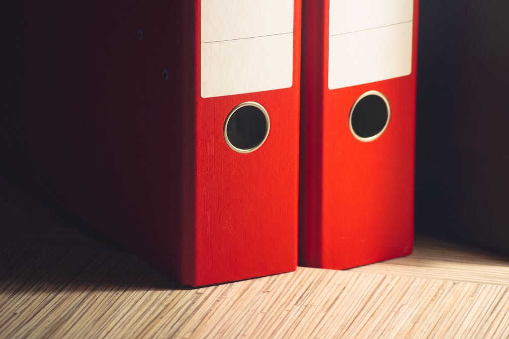 Close-up of two red lever arch files on a wooden desk in a modern office setting.